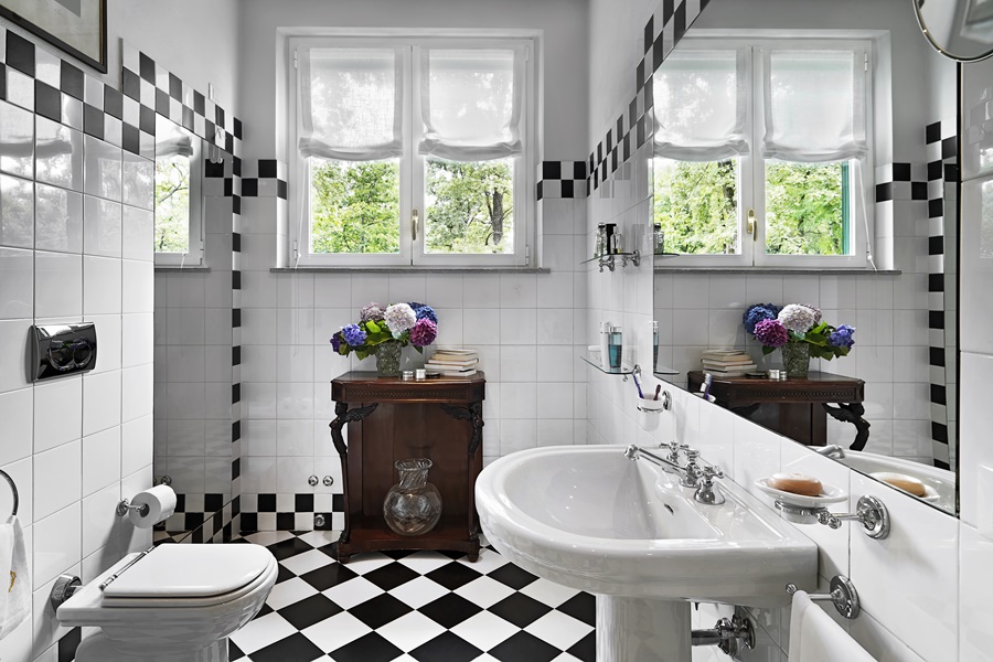Baño vintage con suelo de damero blanco y negro, lavabo con pedestal y mueble clásico de madera. Ejemplo de estilo retro con elementos auténticos.