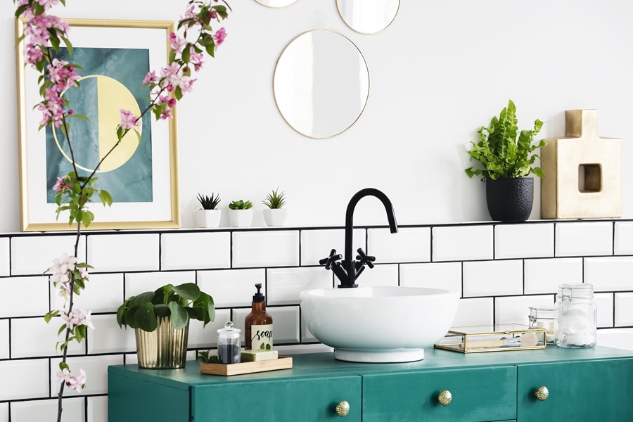 Detalle de baño vintage con mueble verde esmeralda, lavabo sobre encimera y azulejos tipo metro. Estilo retro reinterpretado con grifería negra actual.