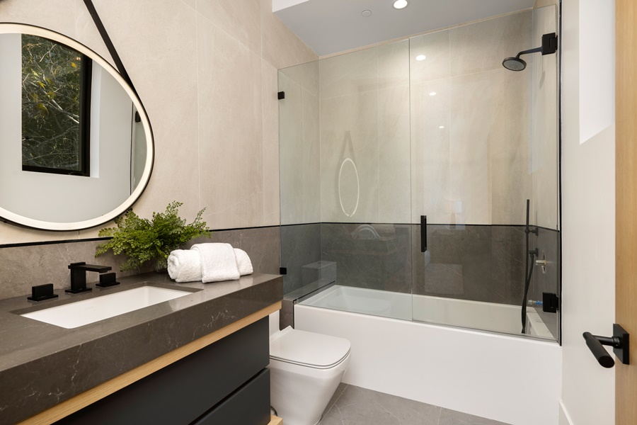 Baño moderno con bañera equipada con mampara de cristal corredera, ideal para ilustrar cómo elegir la mampara de ducha perfecta en espacios pequeños.