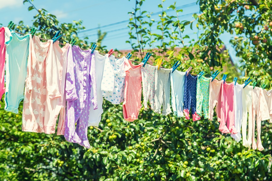 Varias prendas de colores pastel colgadas en una cuerda al aire libre, sujetas con pinzas, muestra de cómo tender la ropa al sol en un jardín